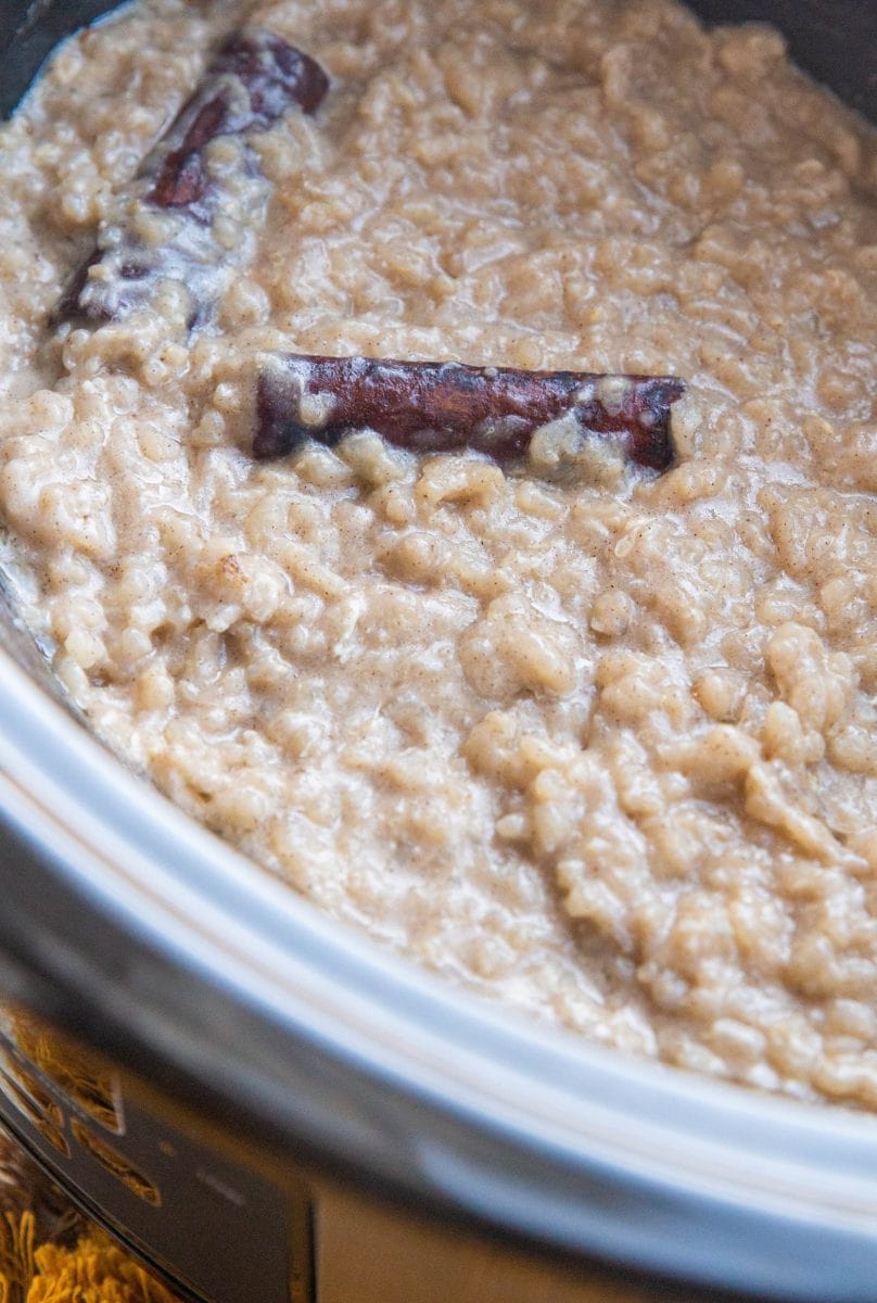 Crock pot with finished rice pudding with cinnamon sticks on top.