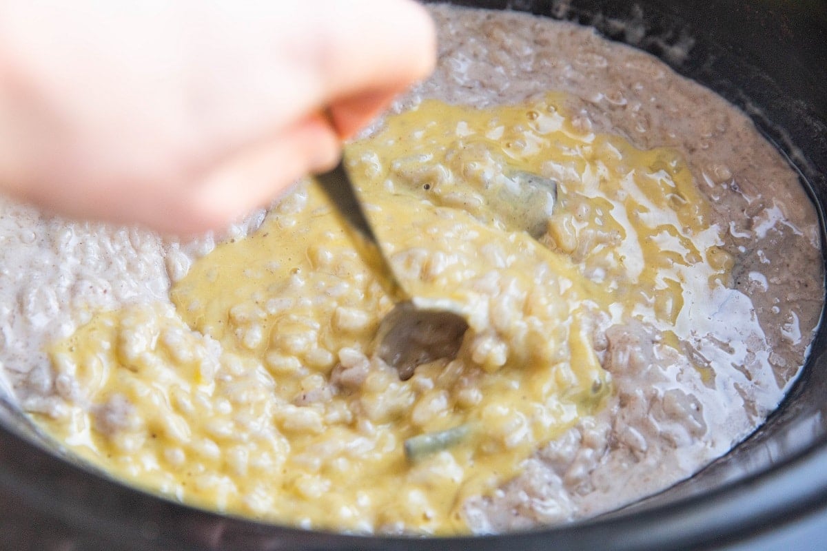 Hand stirring egg mixture into the crock pot with the rice pudding.