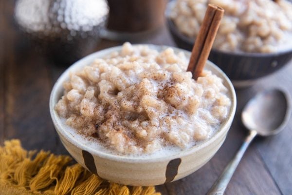 Horizontal photo of two bowls of rice pudding with a cinnamon stick sticking out of the pudding.