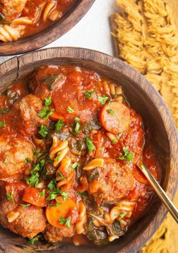 Two wooden bowls of meatball soup on a white background