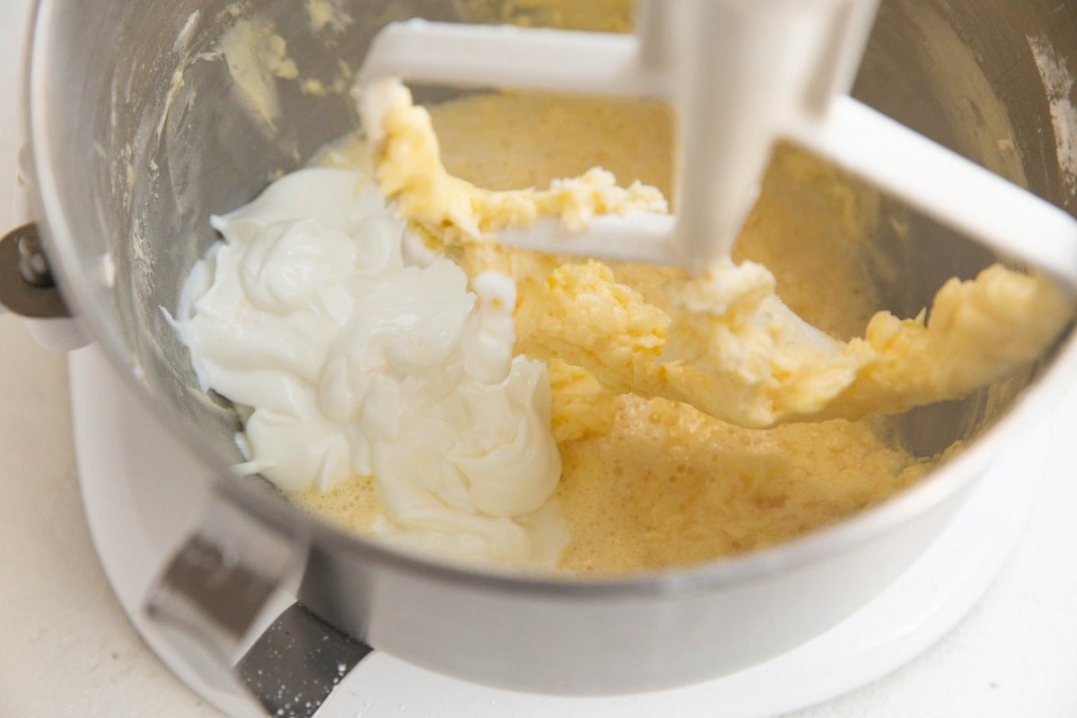Creamy wet ingredients in a stand mixer with the paddle attachment and Greek yogurt added in to be mixed.