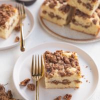 Two white plates with slices of coffee cake on top with a plate of several slices of coffee cake and a cup of coffee to the side.