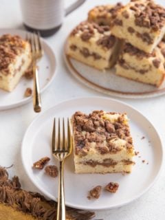 Two white plates with slices of coffee cake on top with a plate of several slices of coffee cake and a cup of coffee to the side.