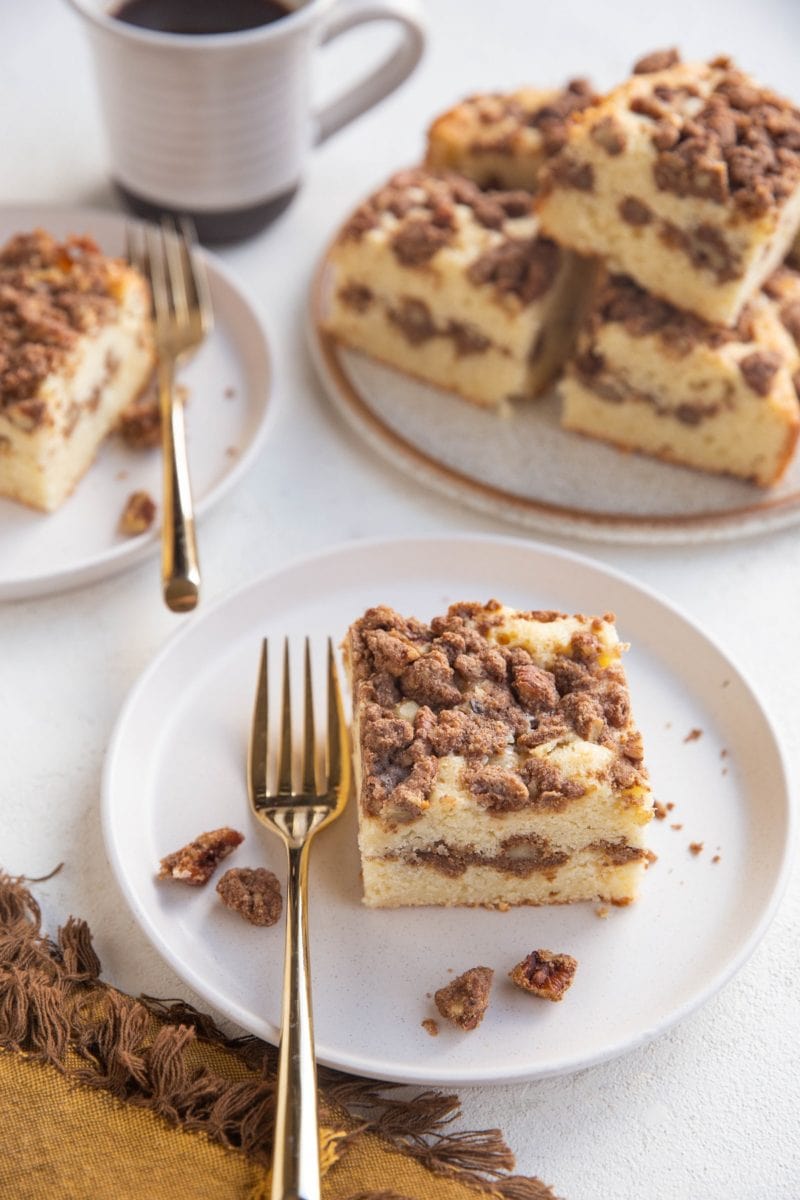 Two white plates with slices of coffee cake on top with a plate of several slices of coffee cake and a cup of coffee to the side.