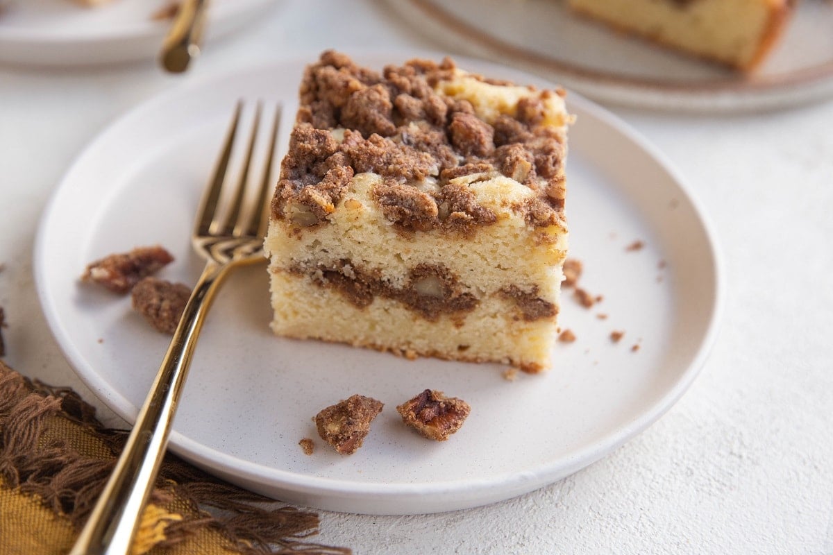 Horizontal photo of a slice of coffee cake on a white plate with a golden fork.