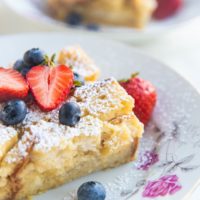 Close up angled shot of two bowls of bread pudding with fruit on top and sprinkled with powdered sugar.