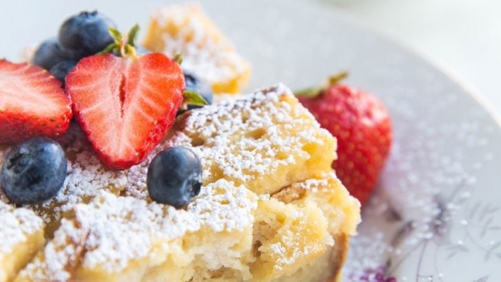 Close up angled shot of two bowls of bread pudding with fruit on top and sprinkled with powdered sugar.