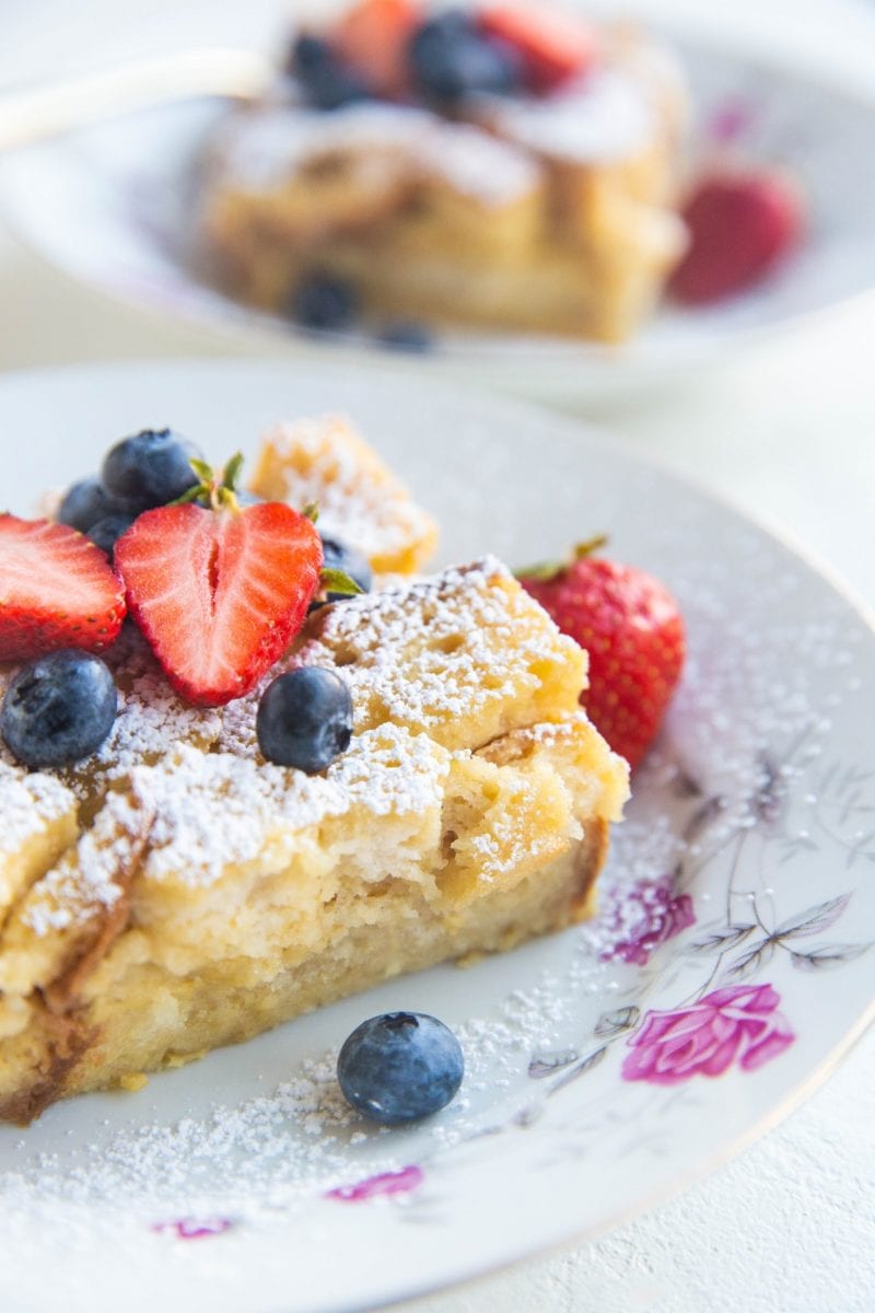 Close up angled shot of two bowls of bread pudding with fruit on top and sprinkled with powdered sugar.