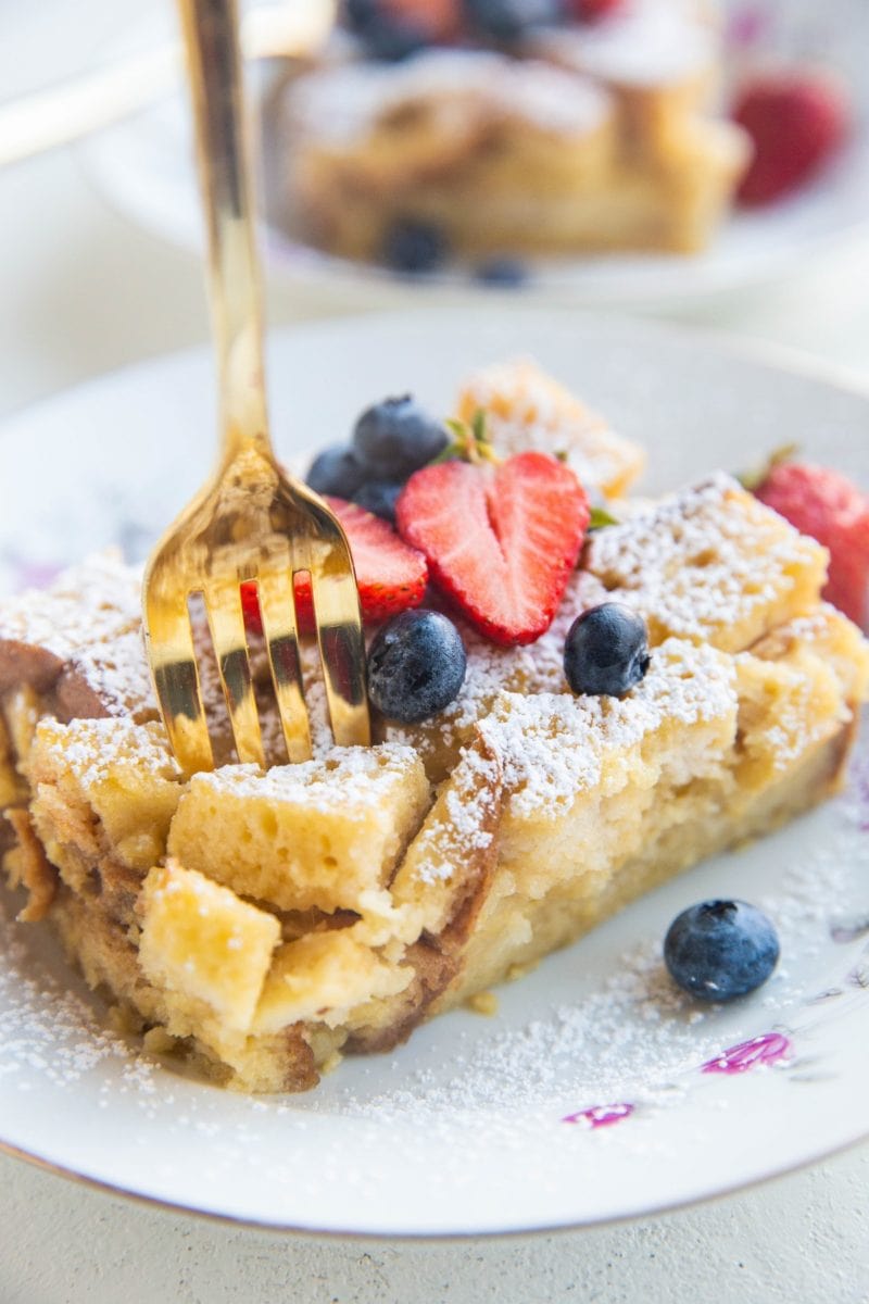 Close up photo of bread pudding in a bowl with a gold fork about to take a bite out.