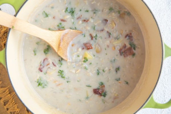 Large soup pot with clam chowder inside and a wooden spoon.
