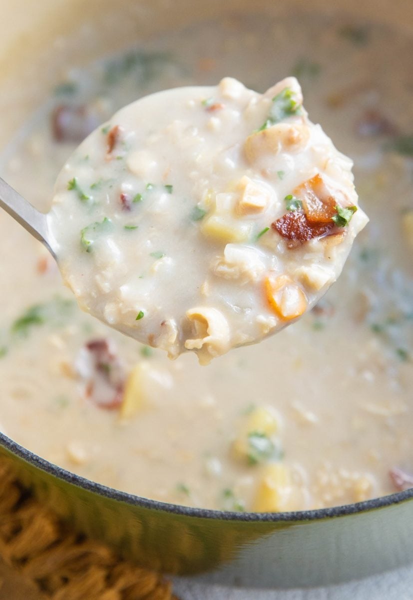 A ladle full of clam chowder taking it out of a soup pot.