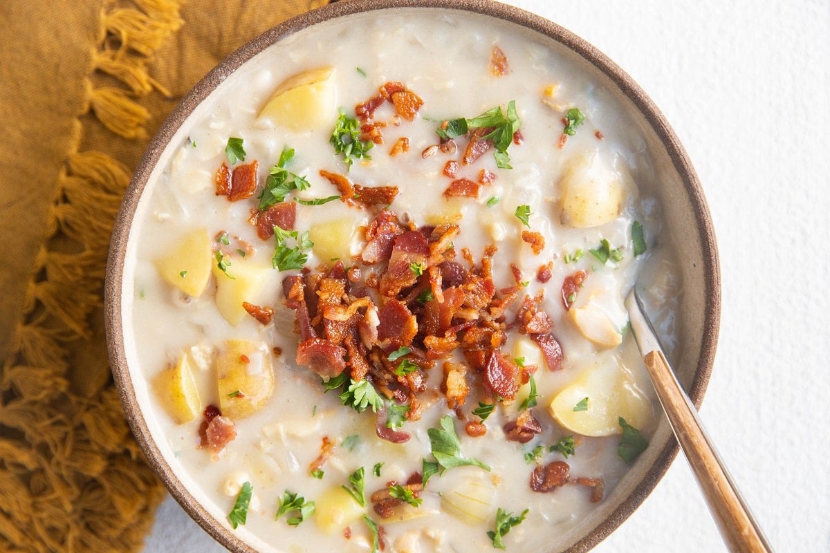 Horizontal photo of bowl of clam chowder with crispy bacon and fresh parsley on top.
