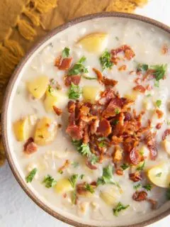 Close up top down photo of clam chowder in a bowl with crispy bacon and fresh parsley on top.