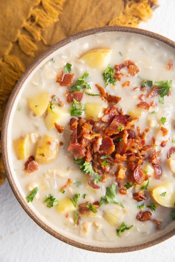 Close up top down photo of clam chowder in a bowl with crispy bacon and fresh parsley on top.