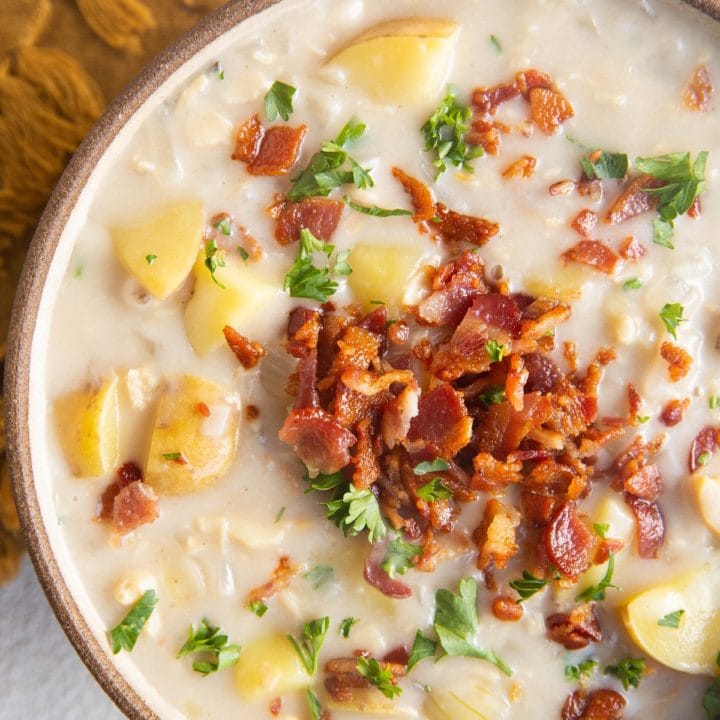 Close up top down photo of clam chowder in a bowl with crispy bacon and fresh parsley on top.
