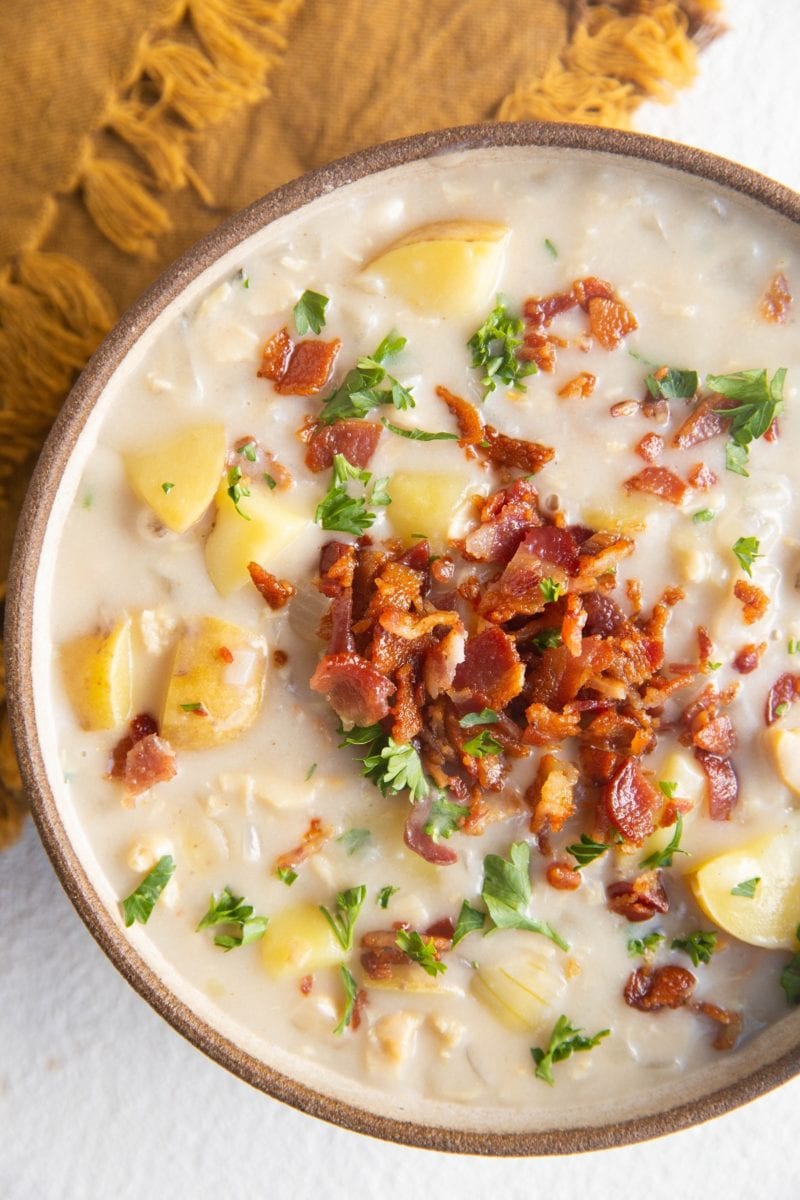 Close up top down photo of clam chowder in a bowl with crispy bacon and fresh parsley on top.