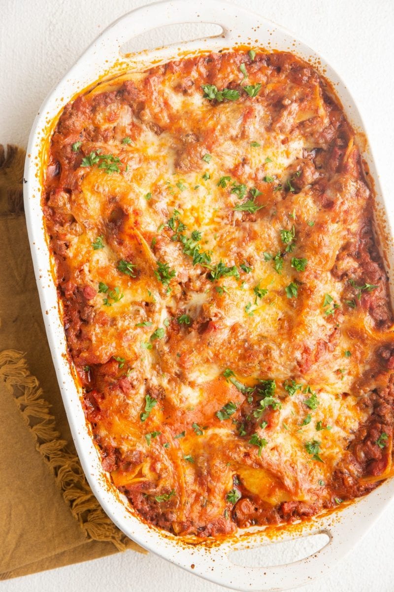 Finished casserole dish of gluten-free lasagna on a white background with a golden napkin to the side.