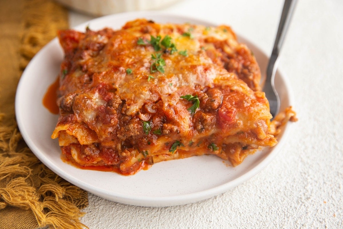 Horizonal photo of a white plate of lasagna with a napkin to the side.