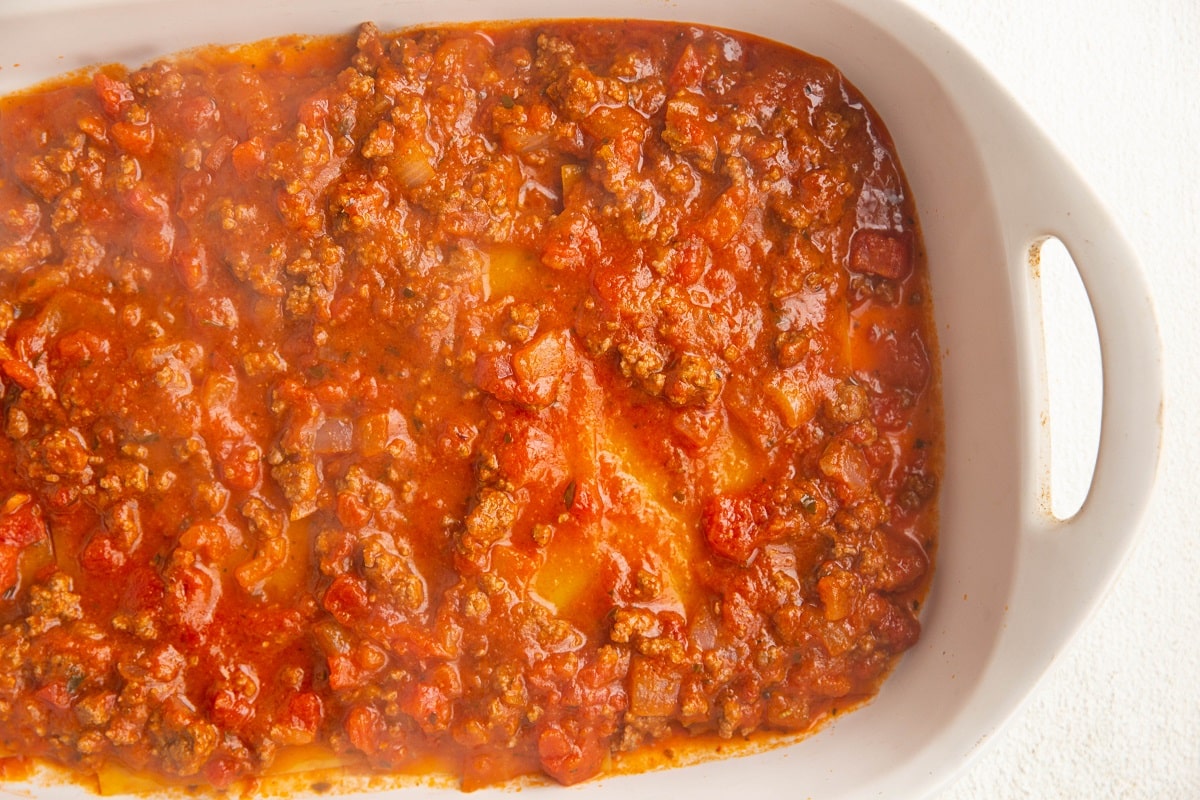 A layer of noodles and sauce in a large casserole dish to make the first layer of lasagna.