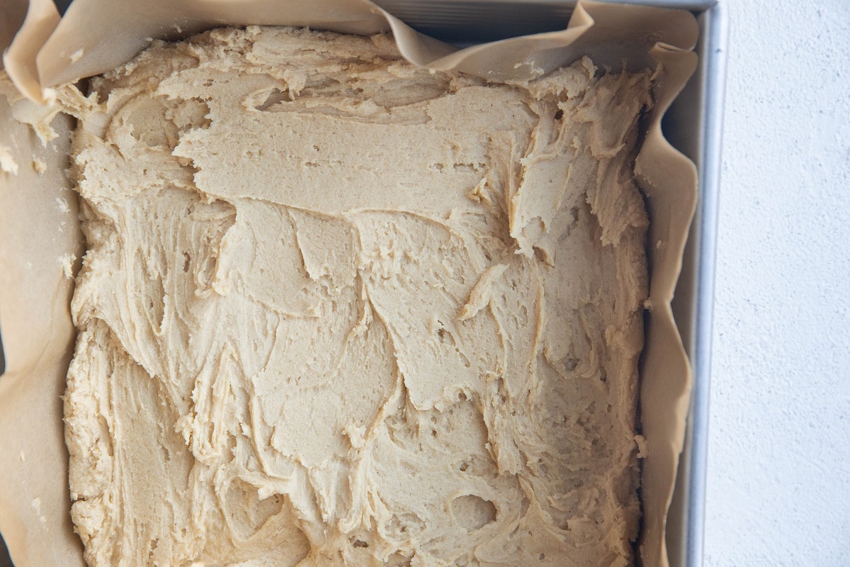 Peanut butter cookie dough spread in an even layer at the bottom of an 8-inch baking pan.