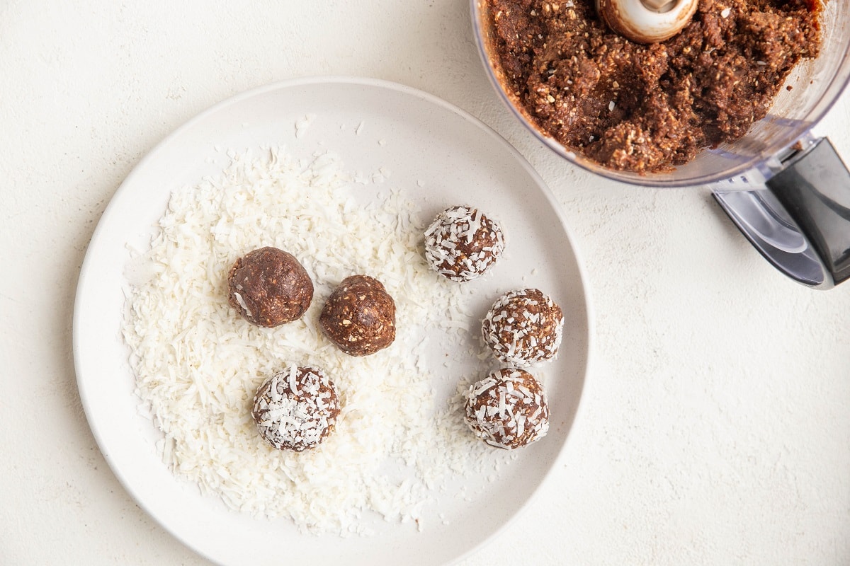 Plate with shredded coconut on it and chocolate snowballs being rolled in the coconut.