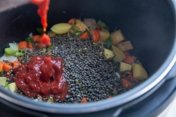 Pouring crushed tomatoes into the instant pot, where there is already lentils and vegetables.