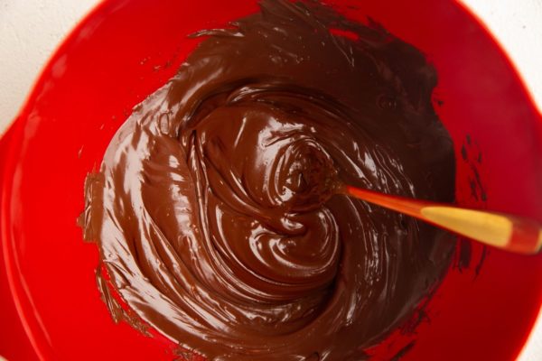 Melted chocolate in a red mixing bowl with a golden spoon.