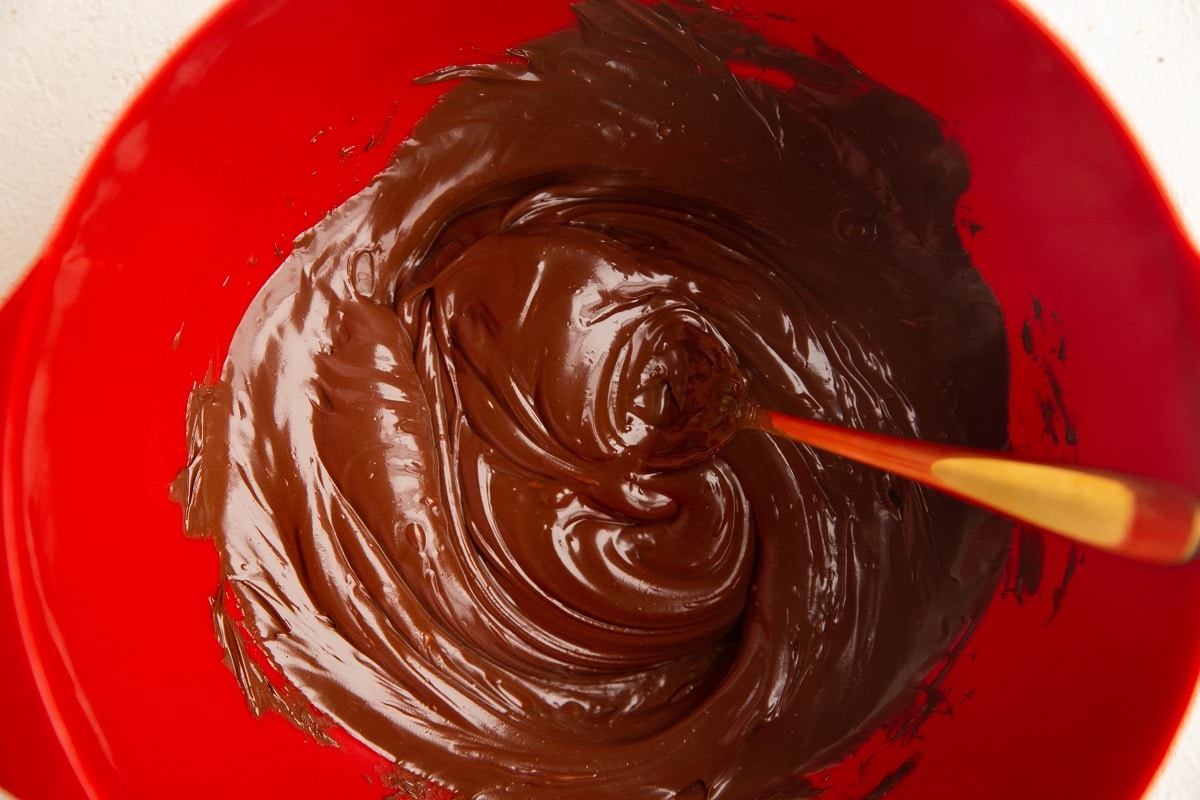 Melted chocolate in a red mixing bowl with a golden spoon.