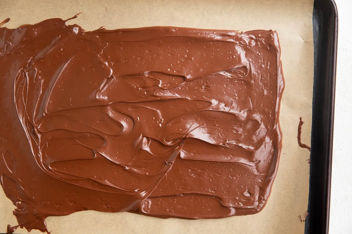 Rimmed baking sheet with melted chocolate spread over a piece of parchment paper into a large rectangle.