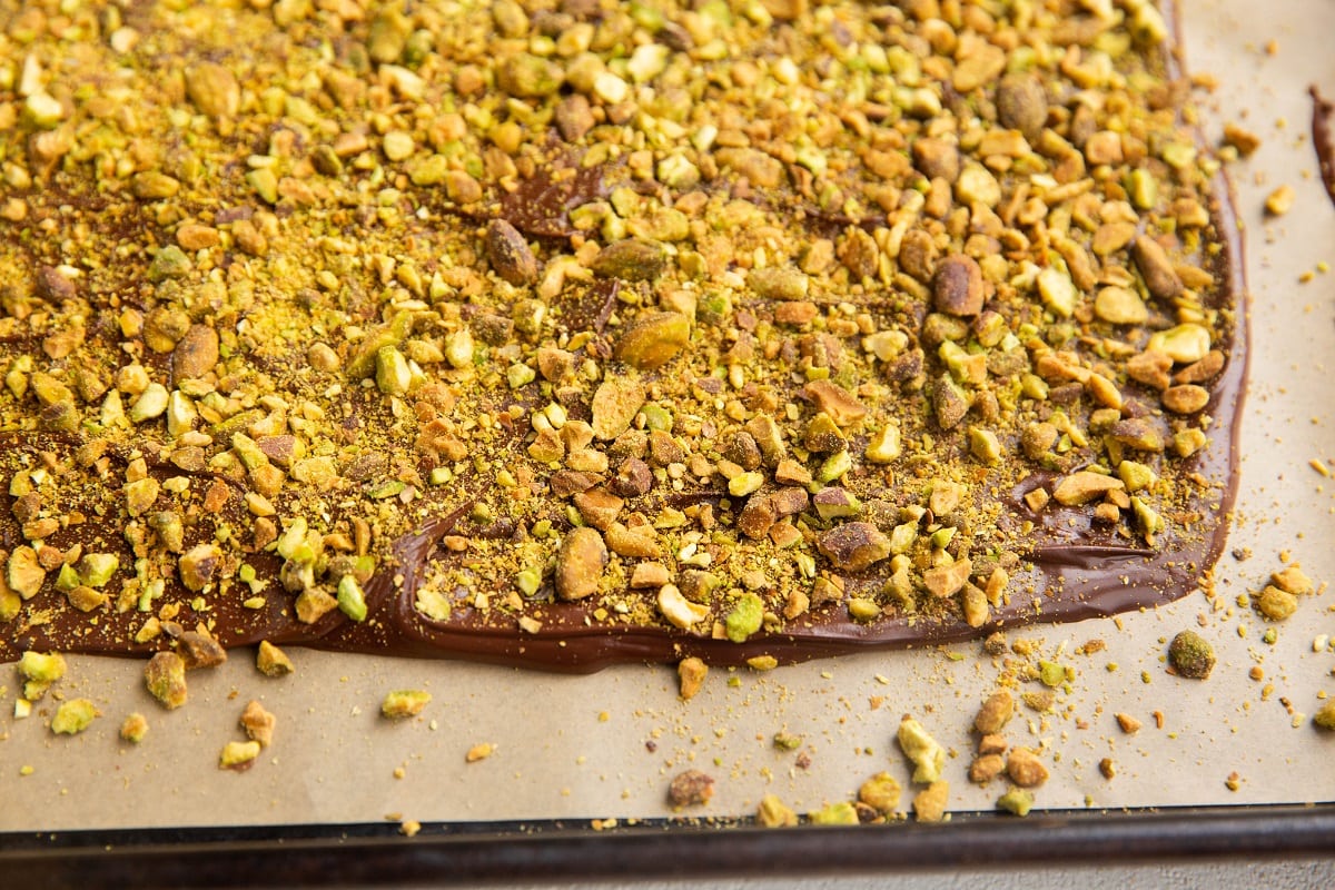 Melted chocolate spread on a cookie sheet with chopped pistachios on top.