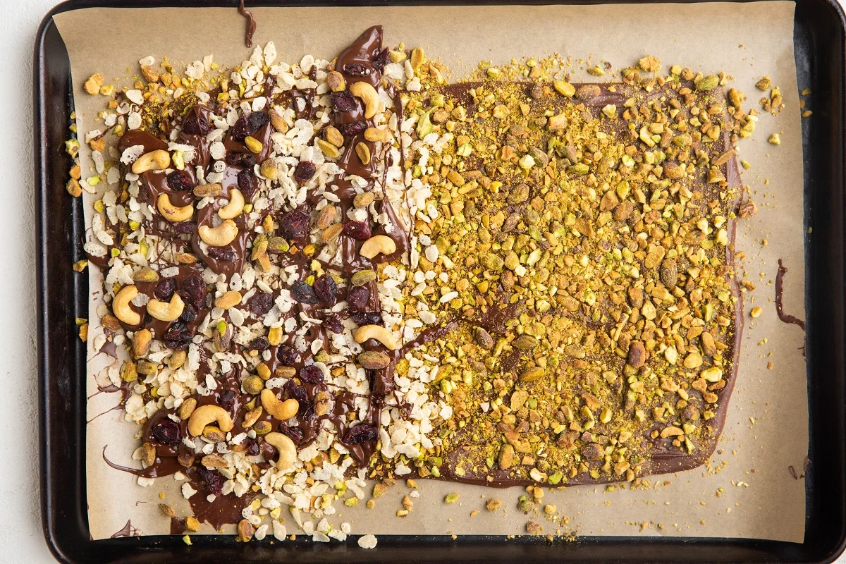 Baking sheet with half pistachio bark, half cashews, dried cranberries, rice cereal.