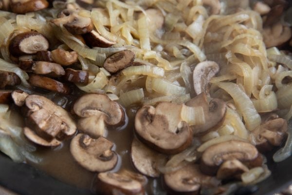 Sauteed onions and mushrooms in a skillet with water coming out.