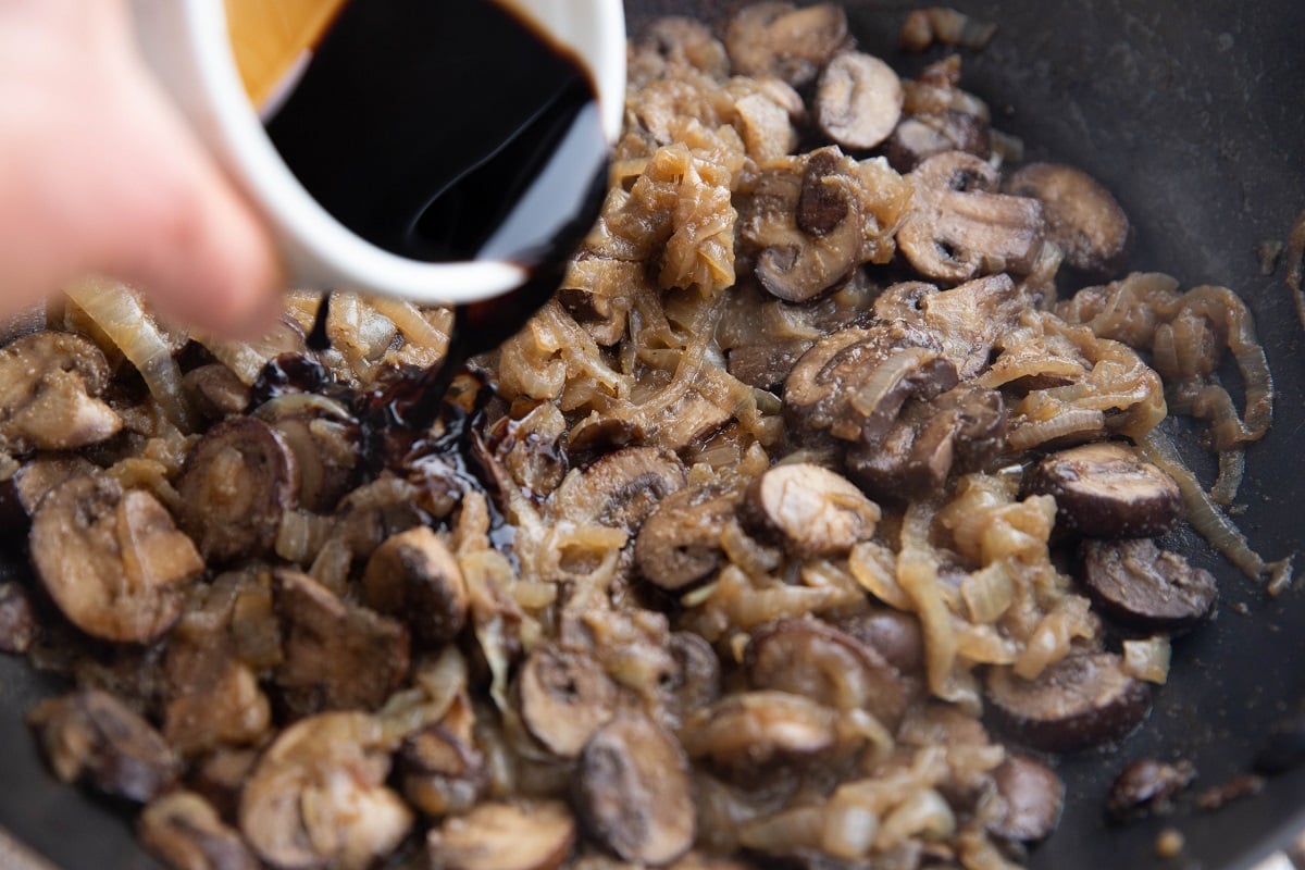 Pouring balsamic vinegar into the skillet with sauteed mushrooms and onions.