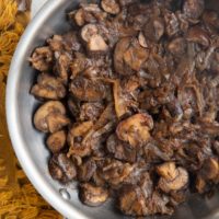 Stainless steel skillet with sauteed mushrooms and onions with fresh herbs to the side.