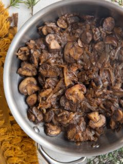 Stainless steel skillet with sauteed mushrooms and onions with fresh herbs to the side.