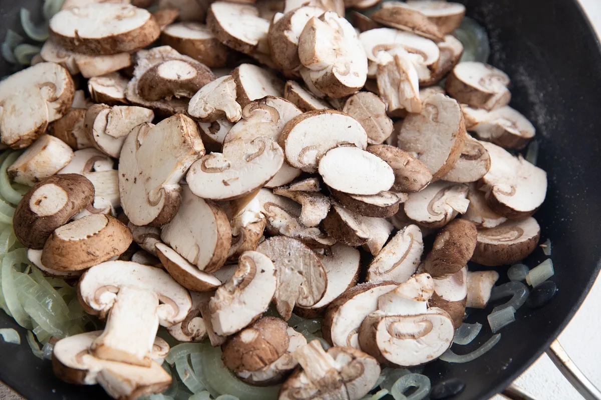 Mushrooms on top of sauteed onions in a skillet, ready to be cooked.