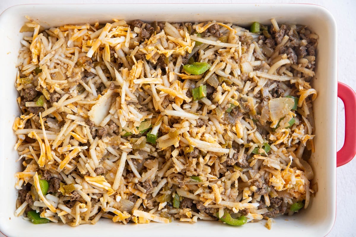 Meat, grated cheese, and hash browns mixed together in a casserole dish.