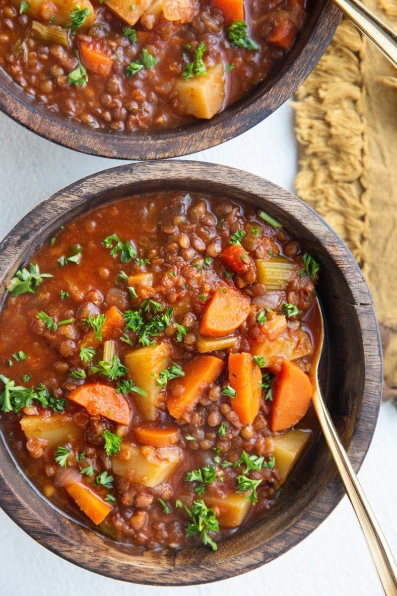 Two wooden bowls full of lentil soup with gold spoons and a gold napkin to the side.