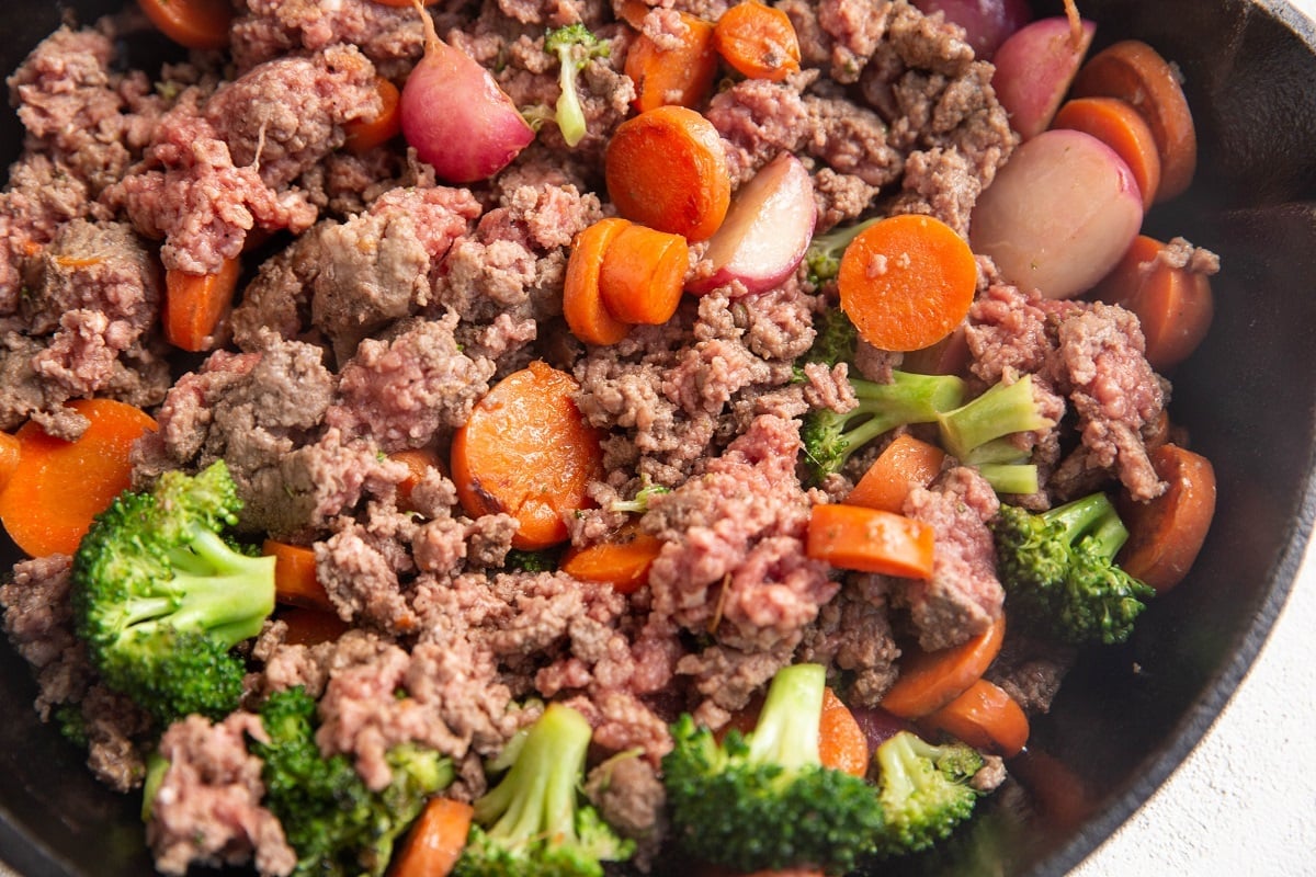 ground beef broken into chunks with vegetables in a skillet.