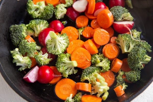 broccoli, carrots, and radishes in a cast iron skillet, sautéing.