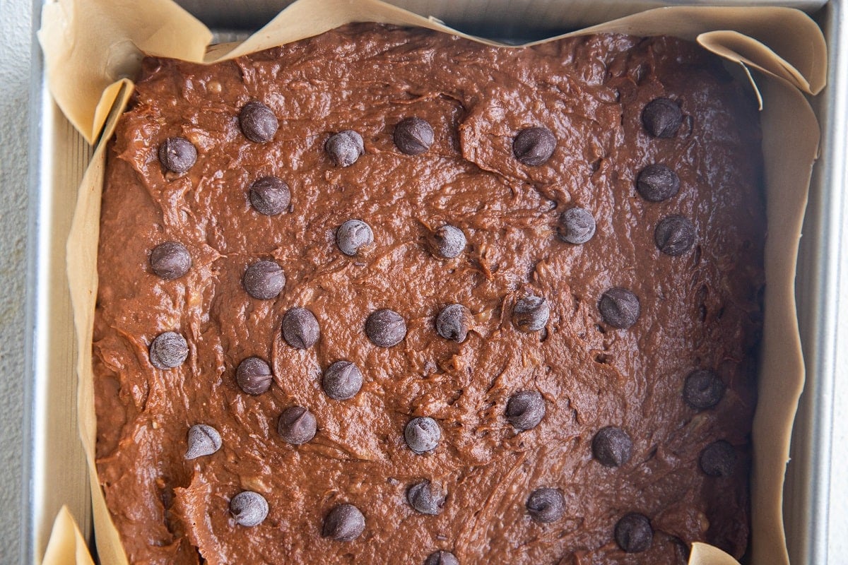Brownie batter in a square pan with chocolate chips on top, ready to go into the oven.