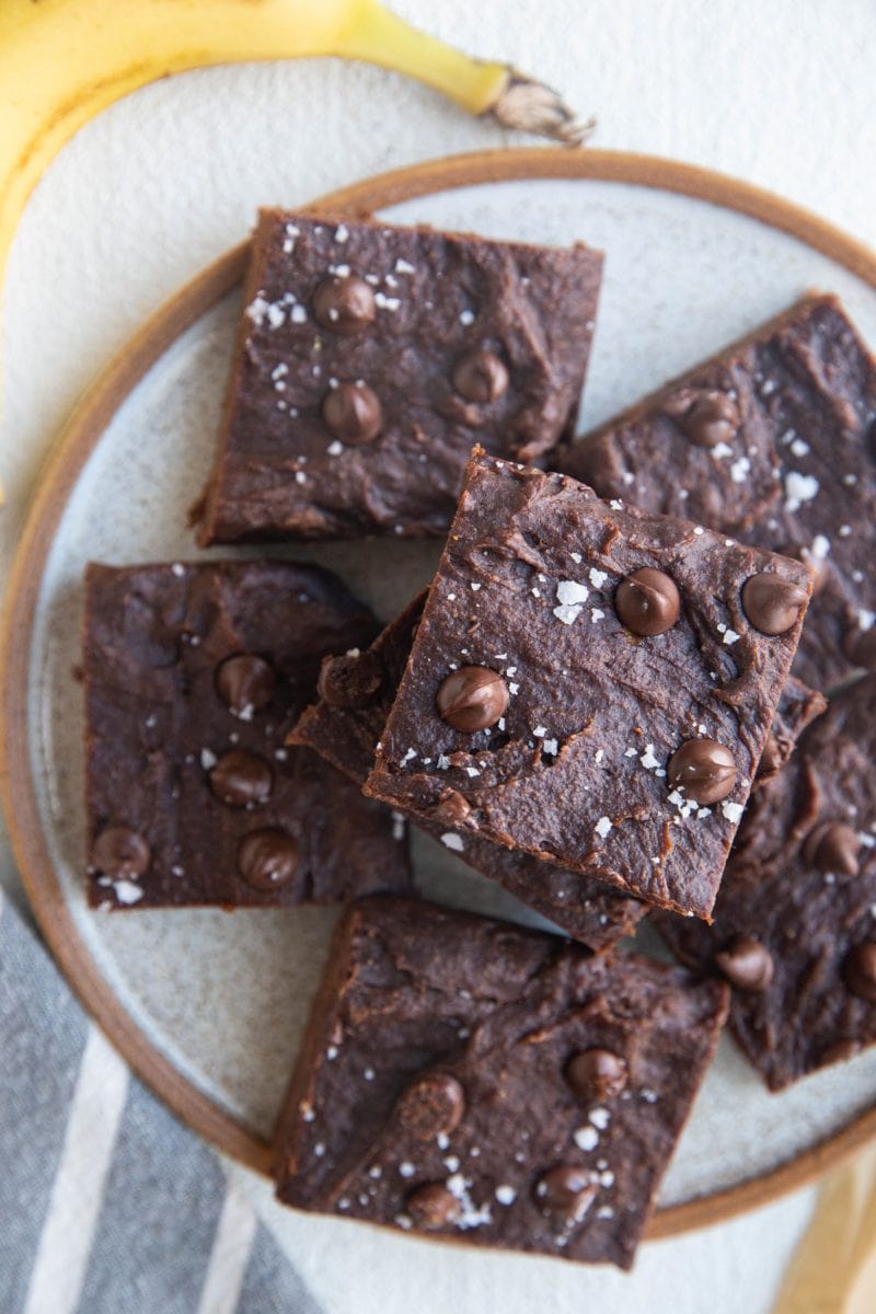 Plate of banana brownies, ready to eat. A banana and a napkin to the sides of the plate.