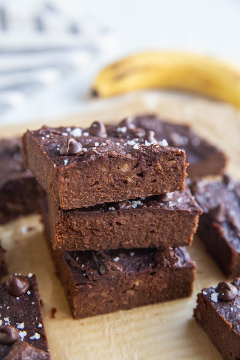 Stack of banana brownies on a sheet of parchment paper with a banana and a napkin in the background.