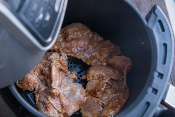 Chicken thighs in an air fryer, ready to air fry.