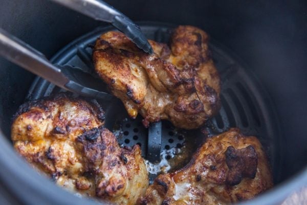 Tongs flipping chicken thighs in an air fryer.