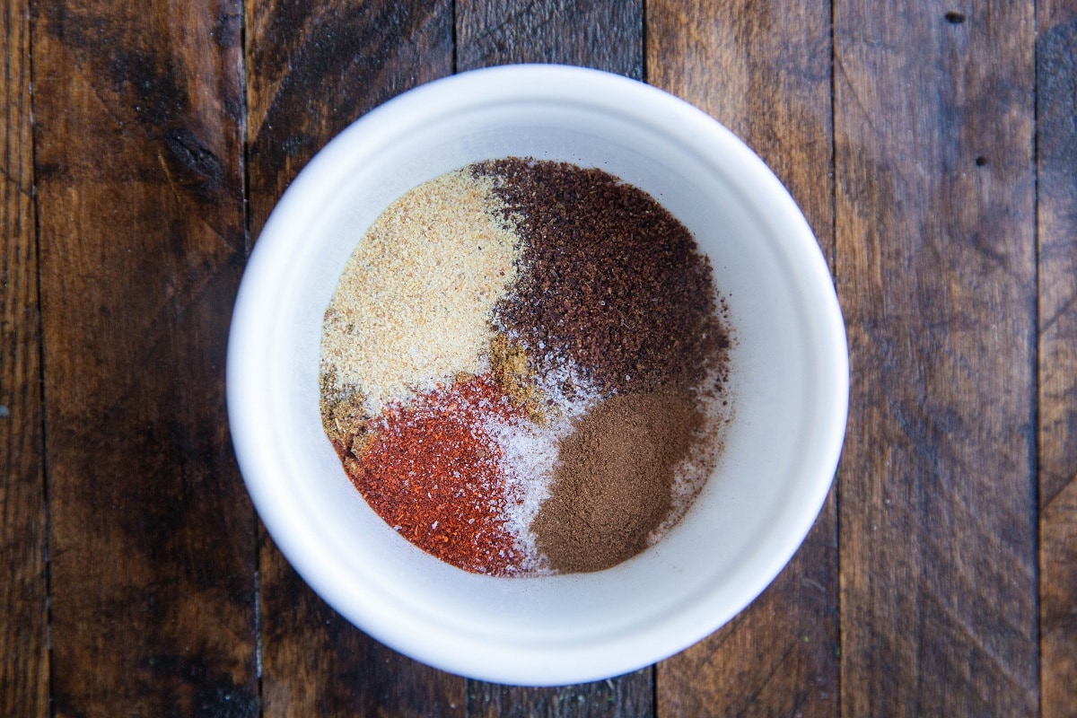 Mediterranean seasonings in a white bowl on a wooden backdrop to make Chicken Shawarma