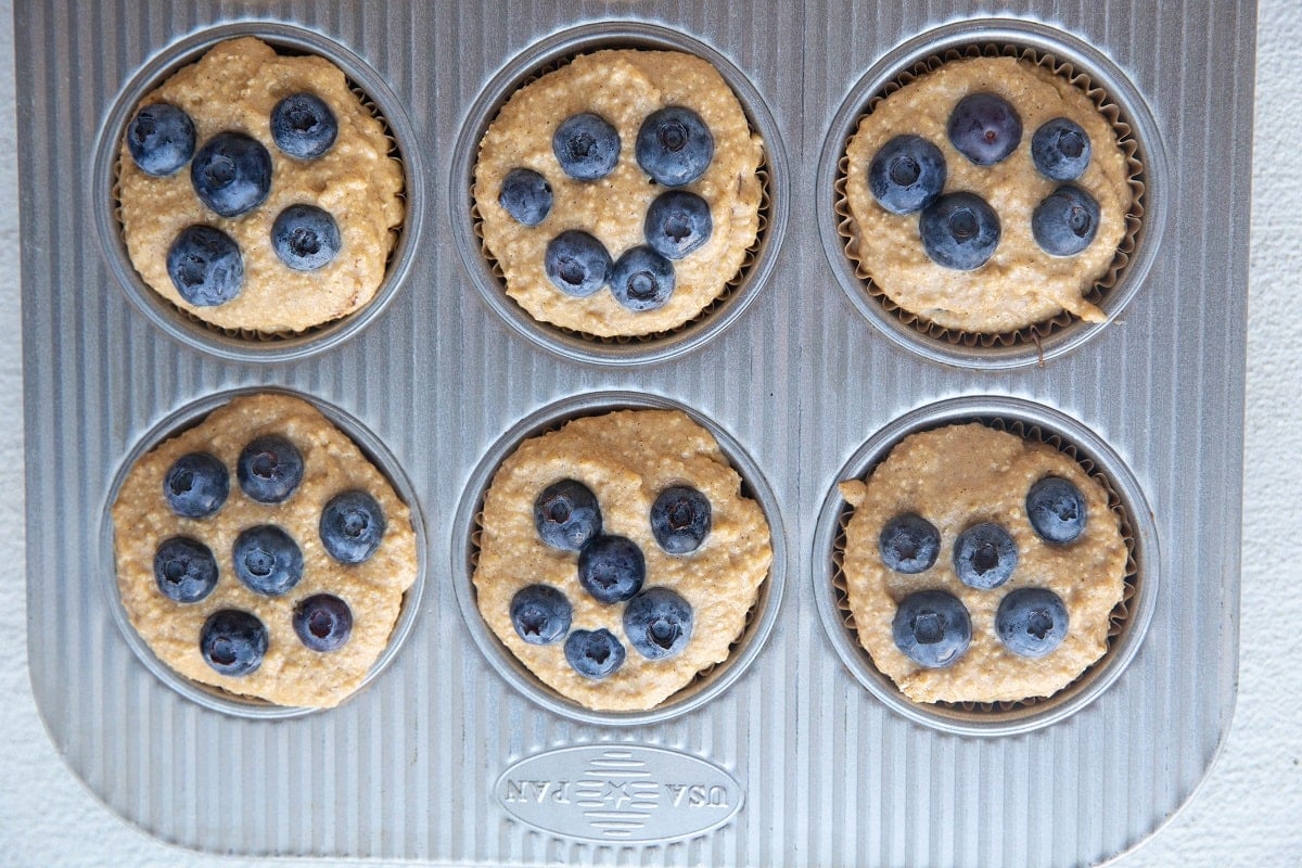 Banana oatmeal muffin batter in a muffin tin with fresh blueberries on top, ready to go into the oven.