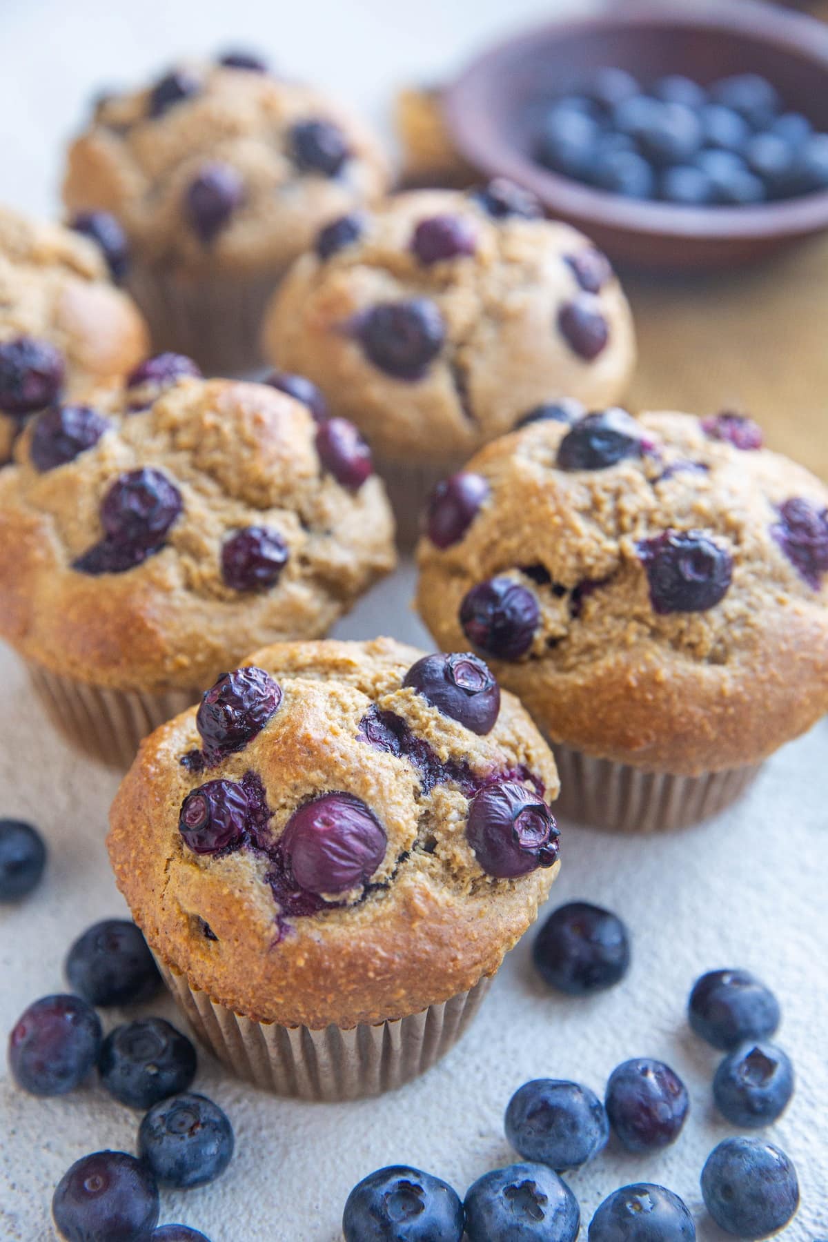 Blueberry muffins sitting on a white backdrop with fresh blueberries all around.