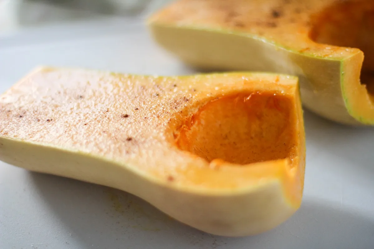 Raw butternut squash cut in half with insides scooped out with cinnamon and salt sprinkled on, ready to go into the oven.