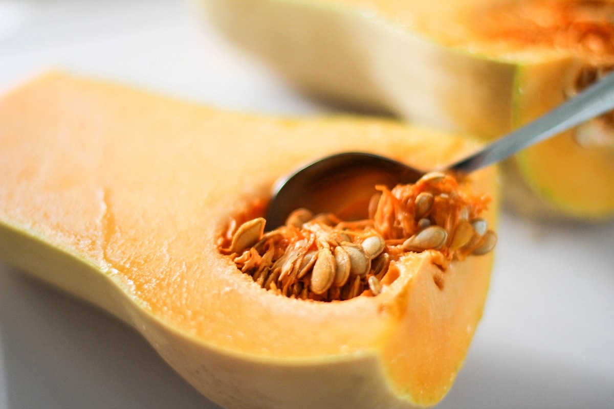 Spoon scooping seeds out of a butternut squash.